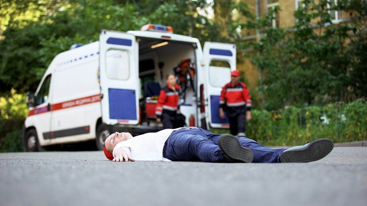 Young man lying on road, paramedics running to victim of car accident, first aid